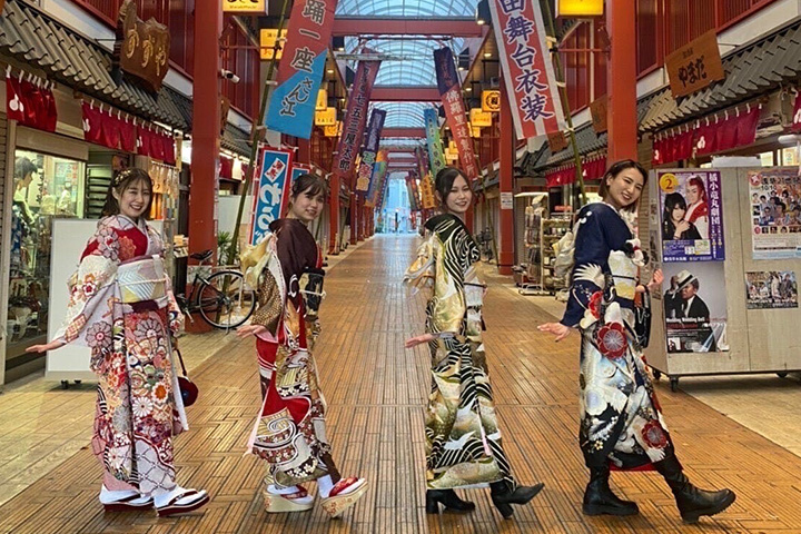 和風の建築のアーケードにて女性4人が着物姿でおそろいのポーズで写っている写真。